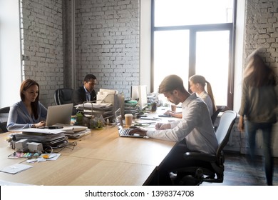Multi-ethnic office workers sitting at shared table working together using computers. Millennial corporate members team diverse people having busy workday. Coworking collaboration and teamwork concept