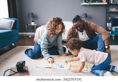 Multiethnic parents with little daughter sitting on carpet and pinning at map while spending time together at home in living room during weekend looking down - Powered by Shutterstock