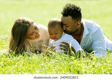 Multiethnic parents and mixed race baby in park. Multiracial family outdoor portrait. Biracial baby child on yard. Diverse family. African american father caucasian mother with baby lying on grass. - Powered by Shutterstock