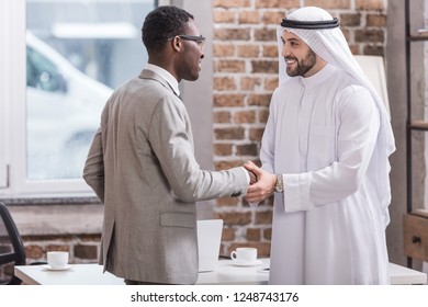 Multiethnic partners shaking hands and smiling in office 