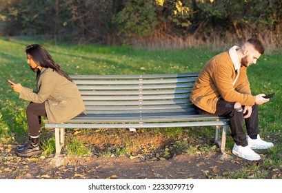 Multiethnic people checking their smartphones sitting on a bench in the park. Smartphone addiction, asociality and social concept obsession - Shutterstock ID 2233079719