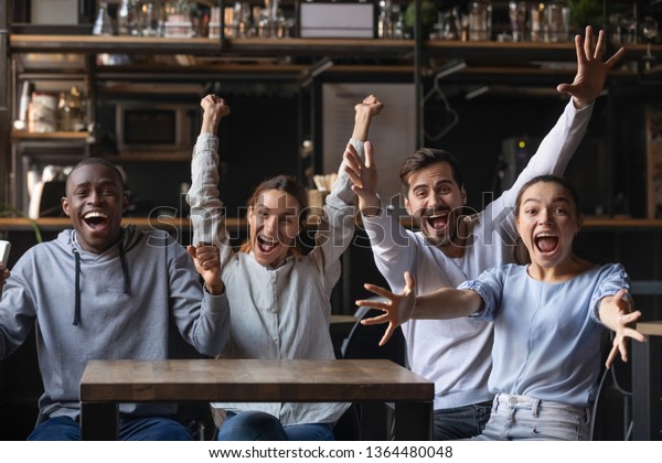 Multi-ethnic people looking at camera sitting at\
cafe public place screaming shouting feels overjoyed happy by\
favourite football club team winning get victory, sports betting,\
lottery winners\
concept