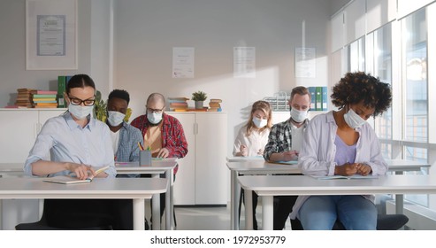 Multiethnic People In Room In Protective Face Mask Attending Lesson In Extension School. Diverse College Students In Safety Mask Sitting At Desk In University Classroom