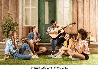 multiethnic people spending time together, man playing guitar while other friends listening - Powered by Shutterstock