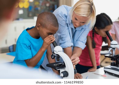 Multiethnic pupils looking through microscope at primary school. Happy elementary students in biology class analyzing cells through microscope. Children with teacher making chemical experiment. - Powered by Shutterstock