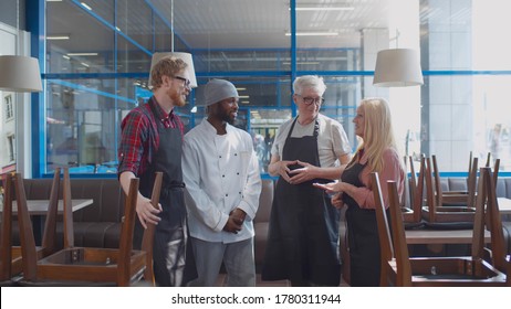 Multiethnic restaurant staff talking before opening. Senior couple owners instructing young chef and waiter before opening coffee shop for customers. Friendly cafe team briefing in morning - Powered by Shutterstock