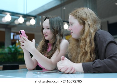 multiethnic school girlfriends using smartphone in corridor during break. Diverse schoolgirls surfing internet on mobile phone together in hallway after classes.  - Powered by Shutterstock