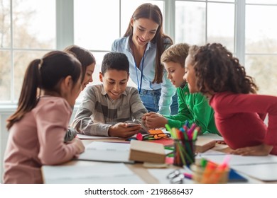 Multiethnic School Kids And Teacher Using Smartphone And Educational Application Learning Sitting At Desk In Modern Classroom At School. Education And Gadgets Concept. Selective Focus