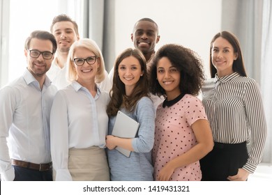 Multiethnic Smiling Businesspeople Standing Looking At Camera Making Group Photo In Office Together, Happy Diverse Employees Posing For Picture With Boss Or Team Leader, Showing Unity And Support