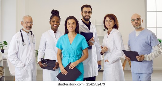 Multiethnic staff in clinic or hospital. Diverse team of happy doctors, general practitioners, specialists and nurses in scrubs and white lab coat uniforms standing in office and smiling at camera