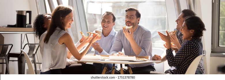 Multiethnic staff gathered together in office kitchen enjoy lunch eat pizza telling funny life stories laughing. Teambuilding corporate party concept. Horizontal photo banner for website header design
