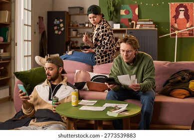 Multiethnic students managing shared expenses in apartment, checking smartphone, calculator, receipts while eating snack. Ideal for student budgeting, roommate finance, cost of living content