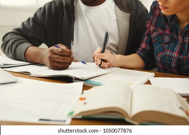 Multiethnic students study together. Black man and caucasian girl working with books, notebooks and laptop, preparing for exams. Teamwork, education and technology concept, crop Stock Photo