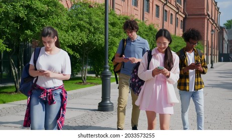 Multiethnic Students Walking Outdoors Using Smartphone. Diverse Young Friends Walk Outside University Building With Mobile Phone