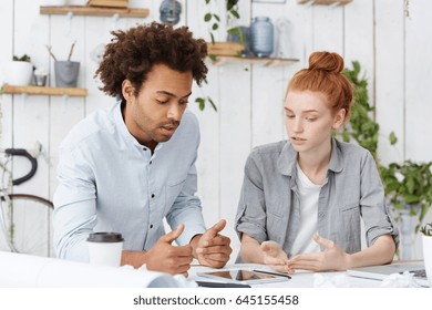 Multiethnic team of creative thinking ambitious young architects brainstorming at white desk, sharing ideas, trying to convince each other while having a dispute or controversy over new project