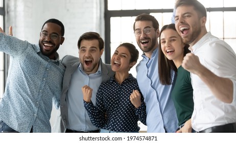 Multiethnic Team Of Excited Employees Celebrating Corporate Achievement, High Sales Result, Work Success, Shouting For Joy. Happy Diverse Professionals Hugging, Laughing, Making Winner Gestures