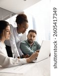 Multiethnic team of focused young managers working on Internet project together, using laptop at office table, discussing online sales strategy, pointing at screen, talking. Vertical shot
