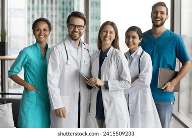 Multiethnic team of happy cheerful young practitioners, surgeons, nurses standing together in hospital office hall, looking at camera, laughing, posing for group portrait - Powered by Shutterstock