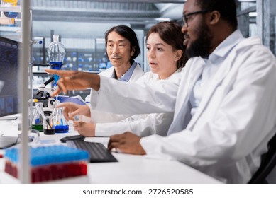 Multiethnic team in laboratory using computer program for DNA data analysis. Diverse research facility coworkers using bioinformatics genomics software on PC in modern lab