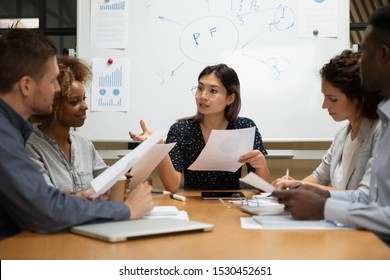 Multi-ethnic team led by asian ethnicity female ceo sitting at boardroom desk holding documents discussing stats, make assess credit worthiness of business, doing financial statement analysis concept