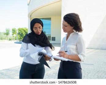 Multiethnic team of managers checking reports outside. Arab and Caucasian business women standing and reading documents. Paperwork concept