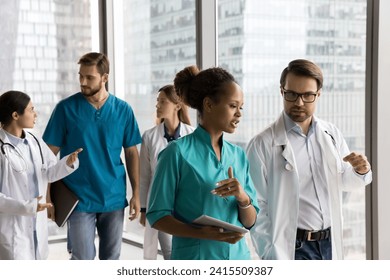 Multiethnic team of medical professionals walking together in hospital office hall. Serious doctor colleagues in white and blue uniforms discussing difficult job cases, career in medicine, teamwork - Powered by Shutterstock