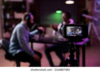 Multiethnic team of people meeting to broadcast internet podcast, recording video discussion on camera. Influencer and guest talking on online livestream to create social media channel content.