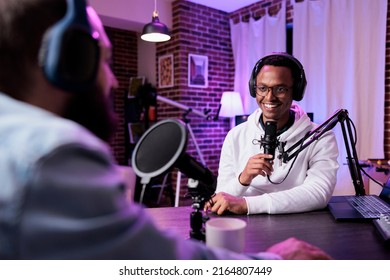 Multiethnic team of people meeting to record podcast episode together, creating online content with live broadcast discussion. Male vlogger talking to adult, livestream production.