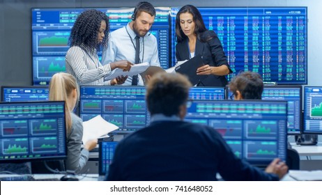 Multi-Ethnic Team Of Traders Is Busy Working At The Stock Exchange Office. Dealers And Brokers Buy And Sell Stocks On The Market. Monitors Display Relevant Infographics, Data And Numbers.