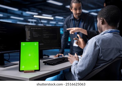 Multiethnic team using green screen tablet to oversee servers used for managing databases. Diverse staff members collaborating while working on mockup device in data center storing information