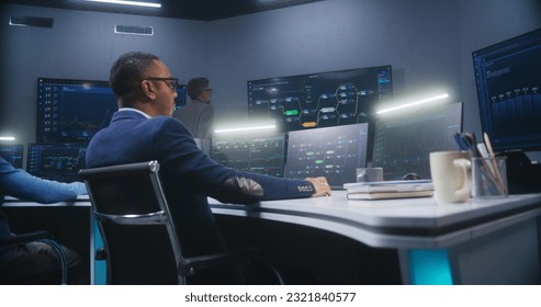 Multiethnic IT technical specialists sit in front of computers with data server in monitoring office. Software engineer works with live analysis charts and blockchain network on big digital screens.