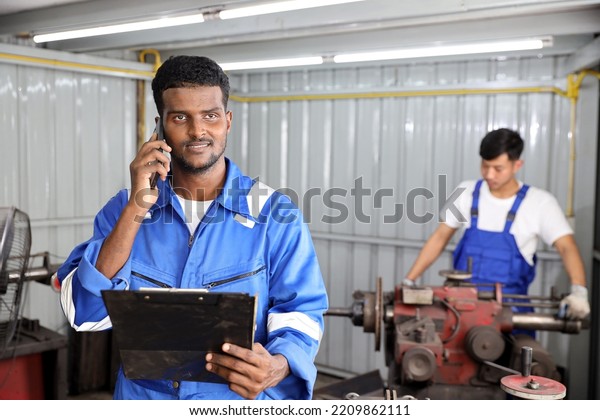 Multiethnic technician mechanic using metal lathe\
machine operate polishing car disc brake with smart mobile phone\
and clipboard at garage. Maintenance automotive and inspecting\
vehicle part\
concept