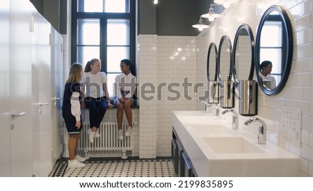 Multiethnic teen girlfriends chat in school bathroom during break. Diverse teenage students gossip in campus toilet after lesson