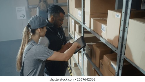 Multiethnic Warehouse Workers Using Tablet Computer, Having Discussion, Scanning Cardboard Boxes with E-Commerce Goods on Shelves with Scanner, Checking Inventory. Sorting Center of Delivery Service.