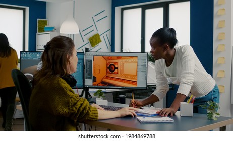 Multiethnic Women Game Designer Looking At Computer With Dual Displays Working Together At Project In Studio Office. Gamer Workers Developing New Online Video Games On Pc With Modern Technology