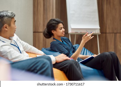 Multiethnic work group talking during informal briefing or meeting, discussing business ideas and sharing thoughts. Comfortable work and relaxation on bean bags chairs. Selective focus
