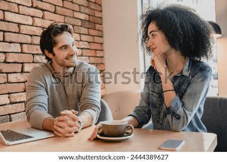 Multiethnic young couple talking while drinking coffee in cafe using laptop. Coworkers colleagues students companions relaxing during shift work break in local cafeteria together