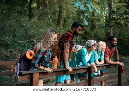 Multiethnic young hikers leaning on wooden fence in forest. Backpackers enjoying in nature. Copy space 