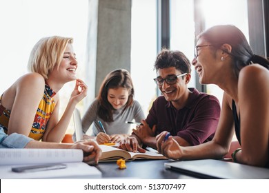 Multiethnic Young People Sitting At Table Reading Reference Books For Study Notes. Group Of Happy Young Students In Cooperation With Their School Assignment.