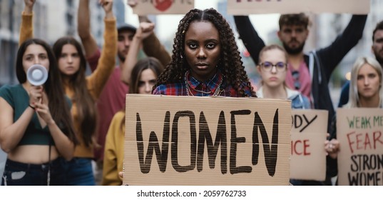 Multi-ethnic young protesters marching for women rights, right to abortion, showing a signboard of Women. African woman in front holding the sign about woman empowerment. - Shutterstock ID 2059762733