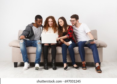 Multiethnic young students study with gadgets, preparing for exam, sitting on sofa in living room, studio shot