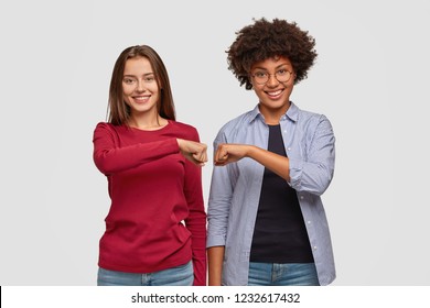 Multiethnic young women give fist bump to each other, show they are friendly team, have positive expressions, demonstrate agreement, dressed in casual clothing. Handshake and friendship concept