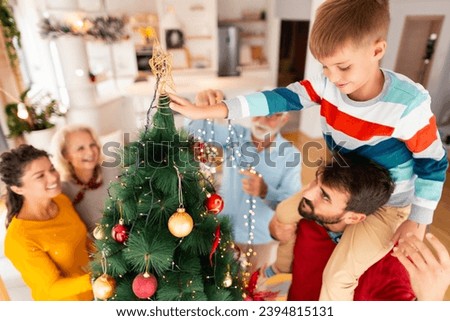 Multi-generation family decorating Christmas tree, father holding son on shoulders to place Christmas star on as tree topper
