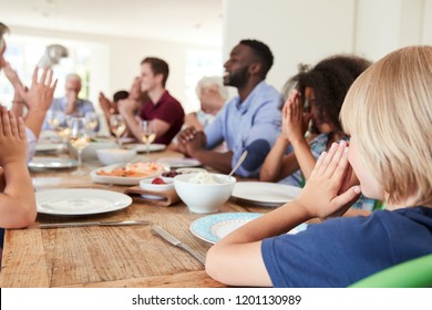 Multi-Generation Family And Friends Around Table Praying Before Meal At Party