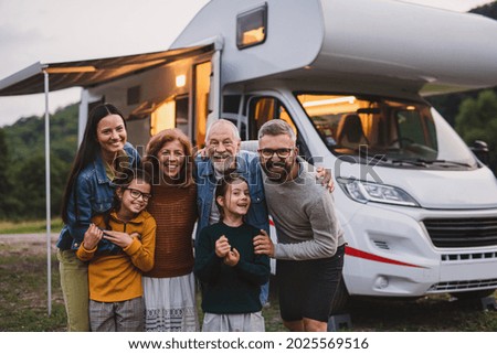 Multi-generation family looking at camera outdoors at dusk, caravan holiday trip.