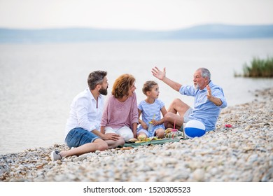 Multigeneration Family On A Holiday By The Lake, Having Picnic.