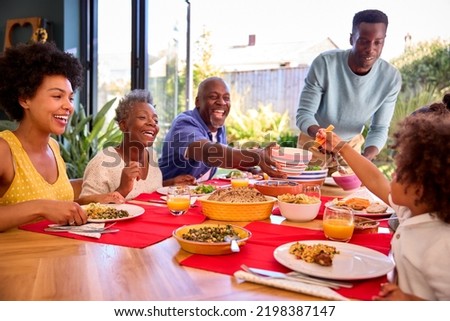 Multi-Generation Family Sitting Around Table At Home Enjoying Meal Together