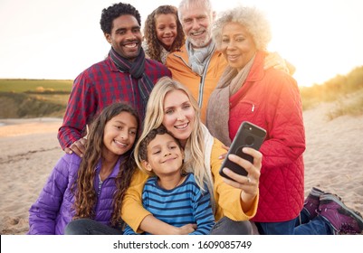 Multi-Generation Family Sitting By Fire On Winter Beach Vacation Taking Selfie - Powered by Shutterstock