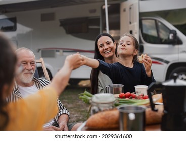 Multi-generation Family Sitting And Eating Outdoors By Car, Caravan Holiday Trip.