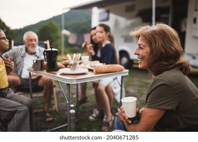 Multi-generation Family Sitting And Eating Outdoors By Car, Caravan Holiday Trip.